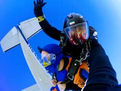 Two skydivers 10,000 feet above the ground with the plane overhead.