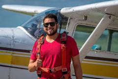 A male Skydiver takes a picture in front of a Cessna.