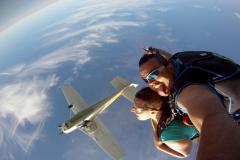 Two skydivers with plane passing overhead.