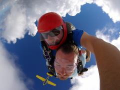 Tandem jumpers descend upside down at 10,000 feet with their plane above.