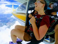 A woman in shorts sits at the cabin door ready to jump into the clouds.