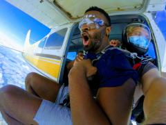 A man wearing shorts sits outside the cabin preparing to skydive.