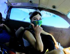 A young women preparing to jump out of a plane gives a thumbs up.