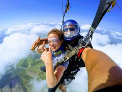 A woman gives two thumbs up as she skydives above the clouds.