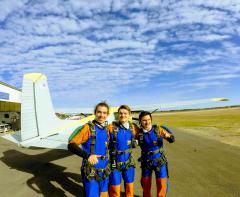 Three skydivers take a picture in front of a plane.